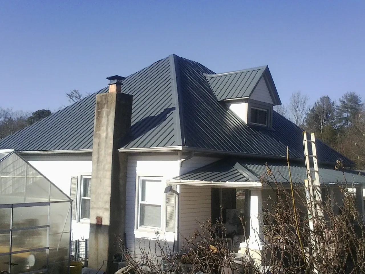 Dark blue standing seam metal roof on a white farmhouse with dormer — Slate & Tile Roof Repair by Roofing Brothers in Rockville