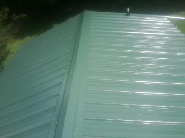 New green metal panels meeting at the ridge of a roof — Flat Roof Repair work by our crew in Rockville