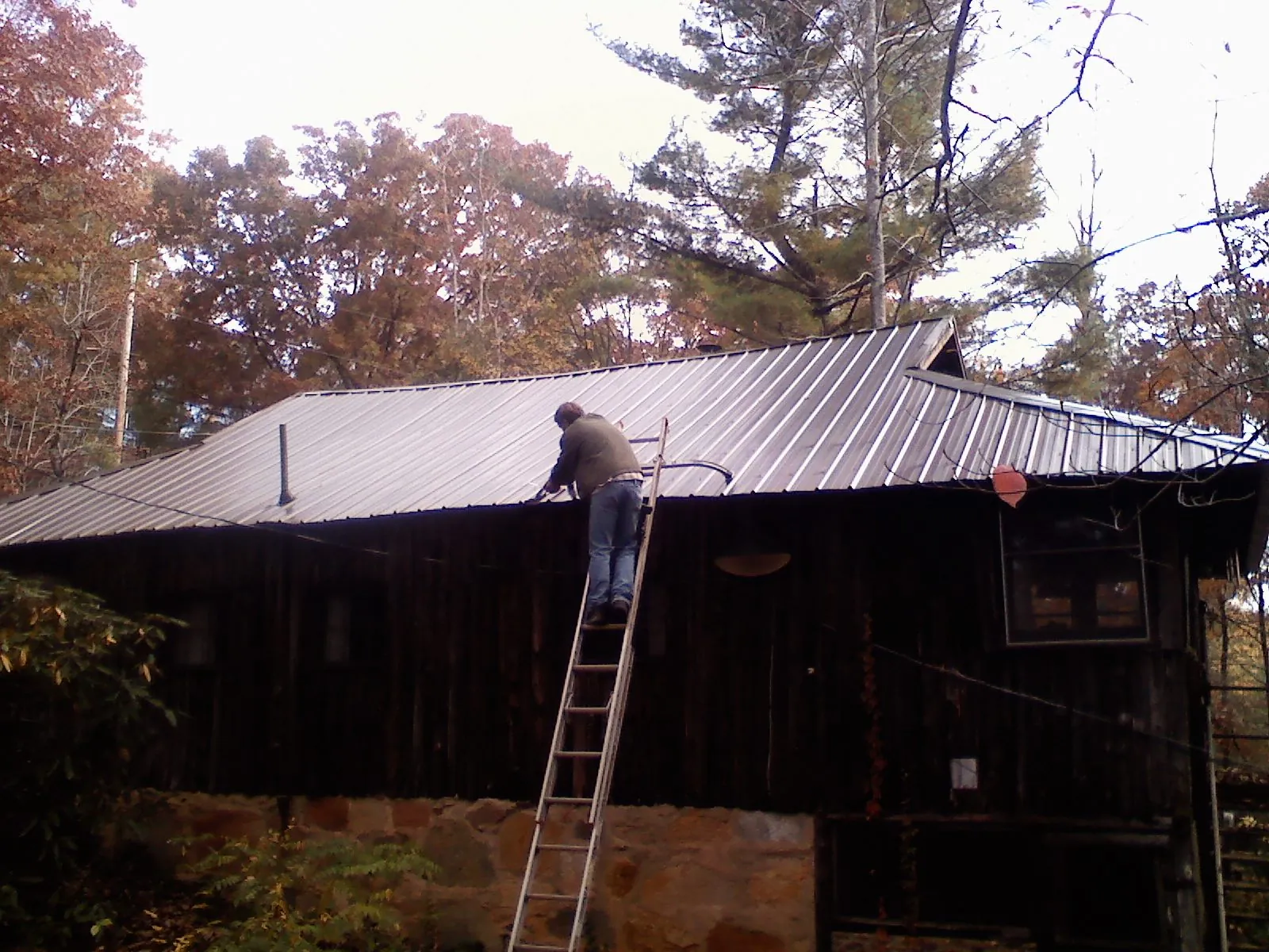 Roofer on a ladder working along the edge of a cabin metal roof in Rockville